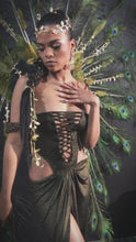 Load and play video in Gallery viewer, Model wears a dark metallic gold dress with a laced corset inspired bodice with a draped skirt. She's styled with a Carnival inspired peacock feather backpack.